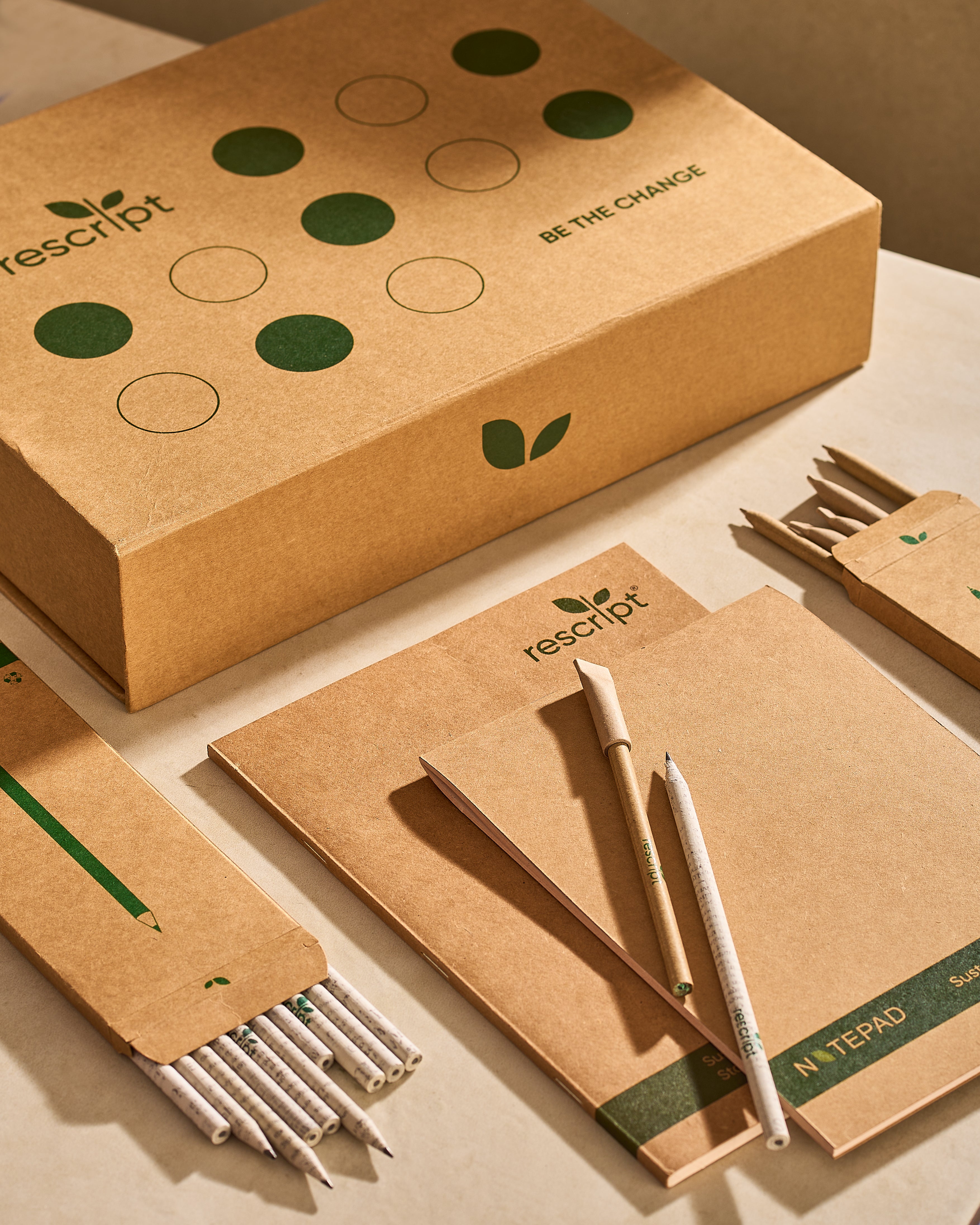 Rescript eco-friendly stationery set including notebooks, pens, and a box on a beige background.