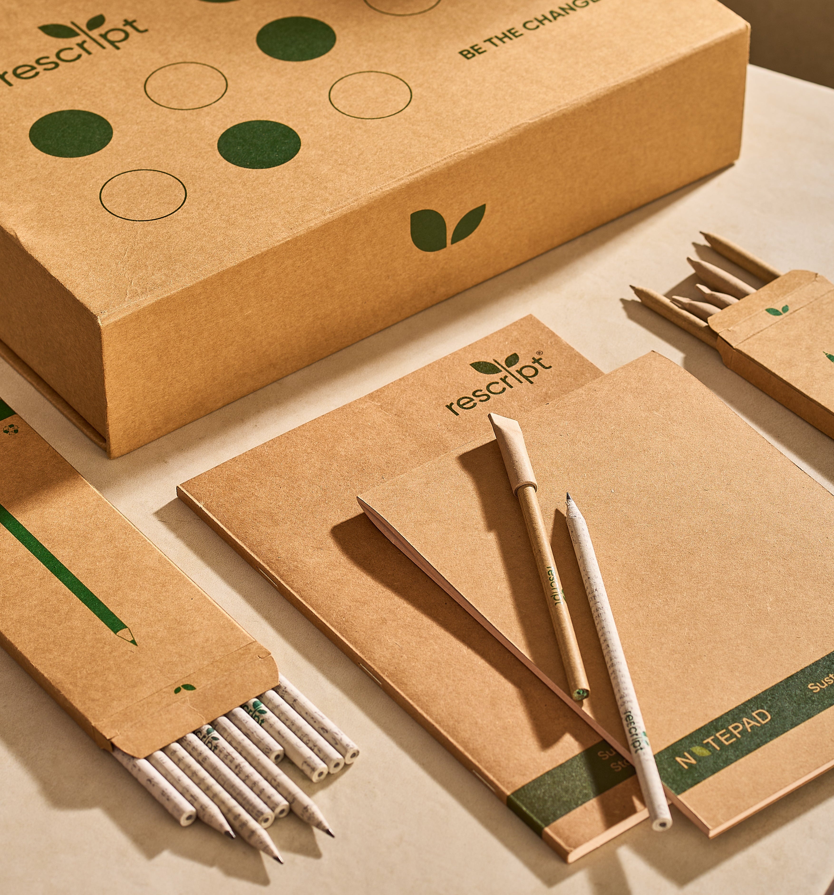 Rescript eco-friendly stationery set including notebooks, pens, and a box on a beige background.