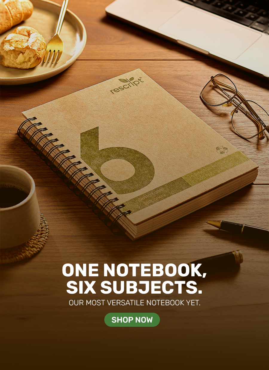 Notebook with Rescribe branding on a wooden desk with coffee, croissant, and glasses.