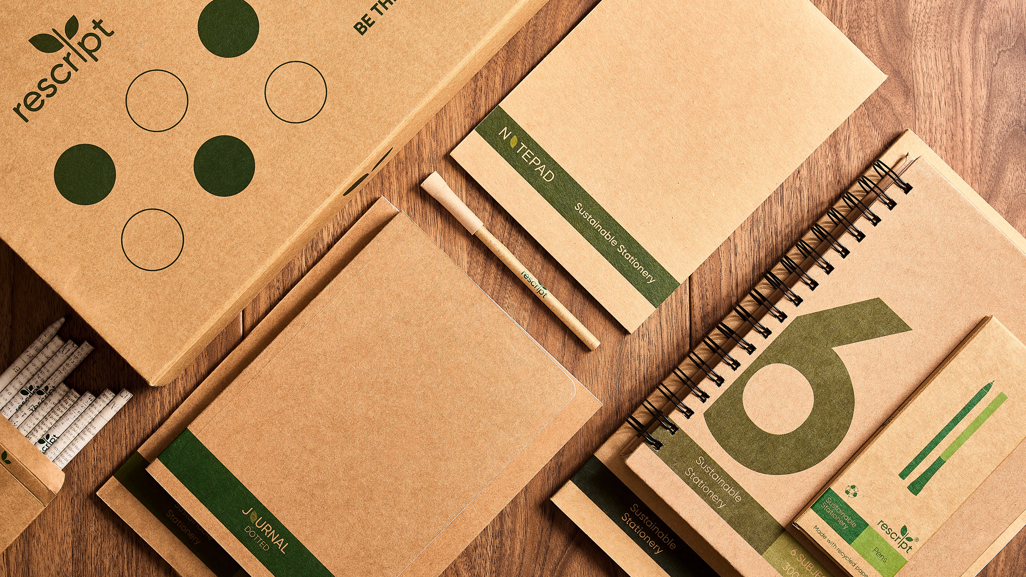 Collection of eco-friendly products including notebooks and a pen on a wooden surface with 'rescript' branding.